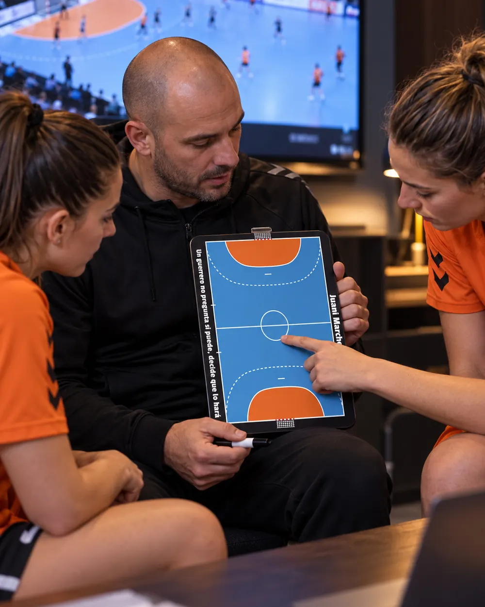 Ein Handballtrainer geht mit seinen Spielerinnen die Taktik an der Taktiktafel durch